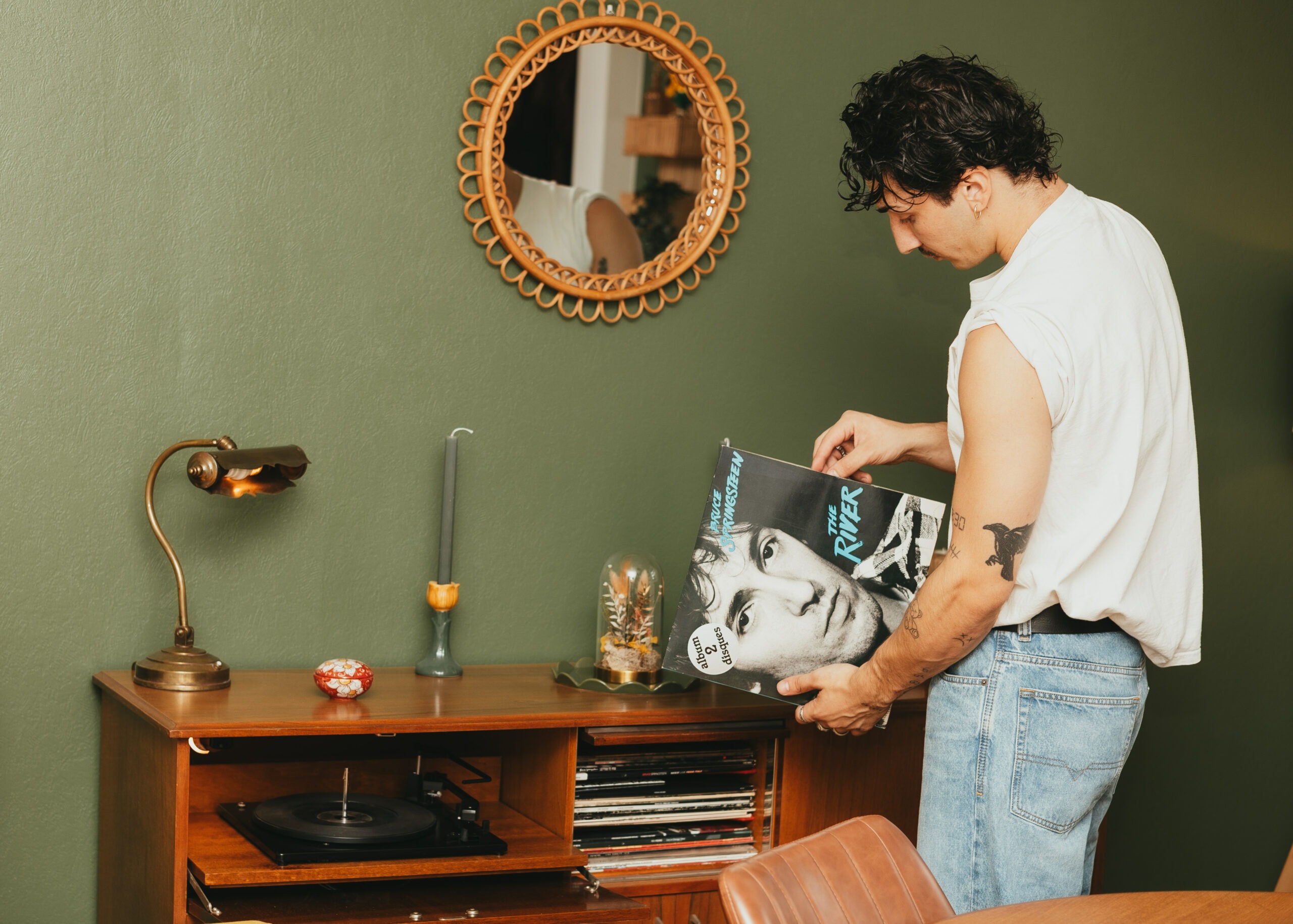 Théo tenant un vinyle de Bruce Springsteen devant un miroir en rotin