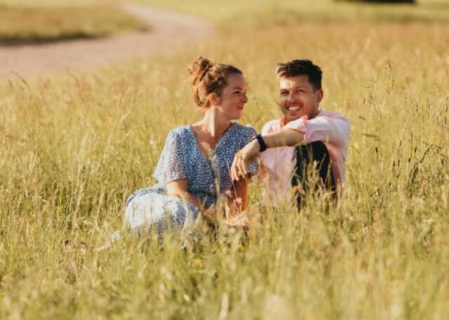 Couple assis dans les hautes herbes, rires complices lors d'une séance photo en Alsace